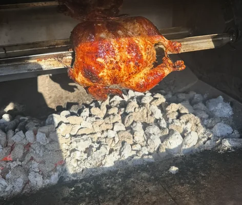 A golden chicken turning on the spit above white-hot charcoal