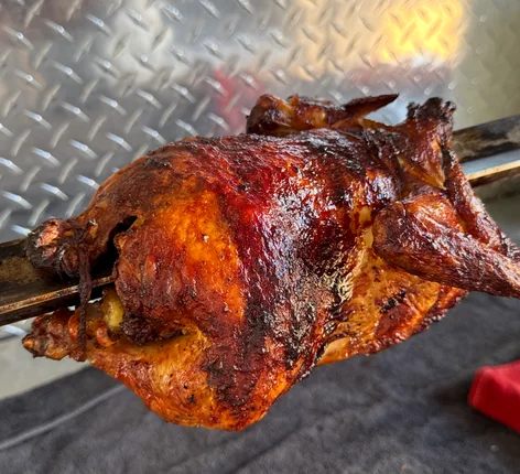A whole chicken on the spit, roasted dark and crispy over charcoal
