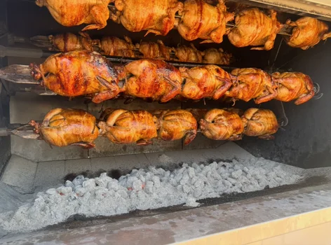 Rows of whole chickens roasting together in the charcoal oven